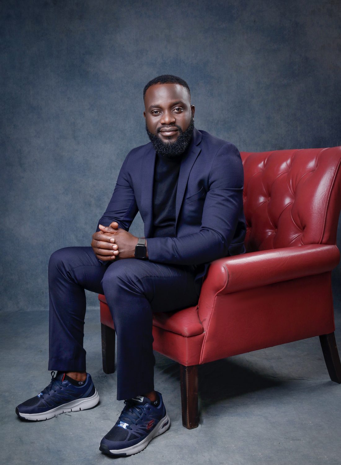 Bisoye Obayan seated in a red armchair, wearing a navy suit